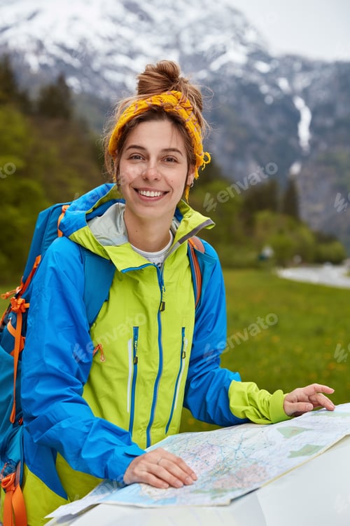 Preview: Delighted Satisfied Active Lady Studies Map, Plans Route In Mountains, Has Glad Expression, Poses