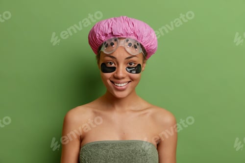 Preview: Horizontal Shot Of Pleased Dark Skinned Woman Smiles Gently Applies Hydrogel Patches Under Eyes To