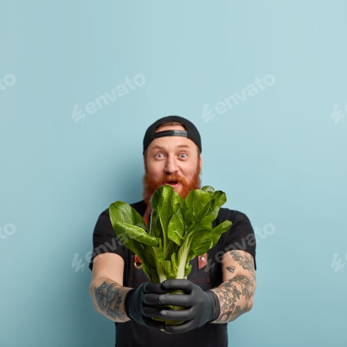 Preview: Idoor Shot Of Surprised Red Haired Man Holds Bok Choy In Both Hands, Shocked With Low Price, Has