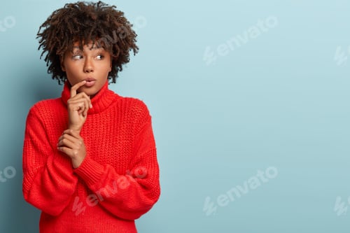 Preview: Studio Shot Of Attractive Woman With Thoughtful Curious Expression, Keeps Finger Near Lips, Listens