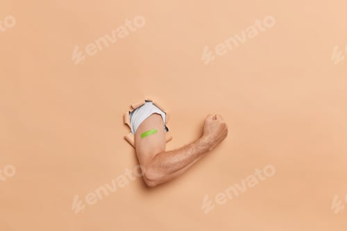 Preview: Unrecognizable Man With Adhesive Plaster On Arm Breaks Through Paper Background Clenches Fist