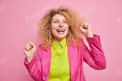 Preview: Happy Upbeat Curly Haired Young European Woman Has Beaming Toothy Smile Makes Triumph Dance