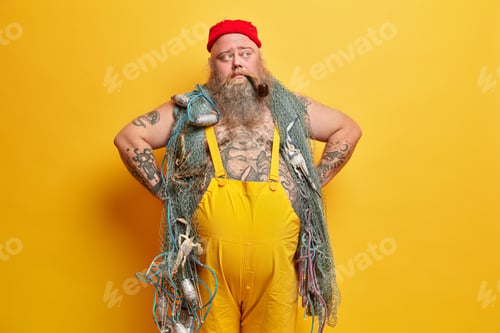 Preview: Thoughtful Boatswain Keeps Hands On Waist Has Fat Belly Wears Red Hat And Yellow Overalls Looks