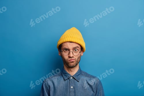 Preview: Embarrassed Unshaven Man Looks With Frownig Displeased Face Expression At Camera, Wears Optical