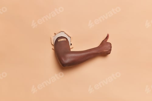 Preview: Horizontal Shot Of Dark Skinned Faceless Man Shows Arm With Plaster After Vaccination Keeps Thumb