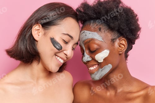 Preview: Studio Shot Of Happy Two Young Women Keep Eyes Closed Apply Clay Mask On Face For Rejuvenation