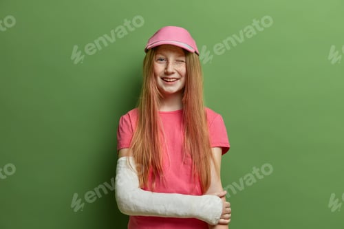 Preview: Children And Health Care Concept. Cheerful Redhead Girl Poses With Broken Arm In Cast, Got Injury