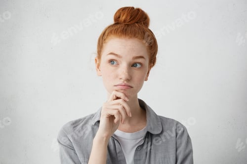 Preview: Portrait Of Charming Young Red Haired Lady Looking Away With Doubtful Expression, Holding Hand On