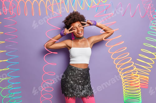 Preview: Positive Stylish Dark Skinned Young Woman Makes Disco Sign Over Eyes, Foolishes Around, Smiles