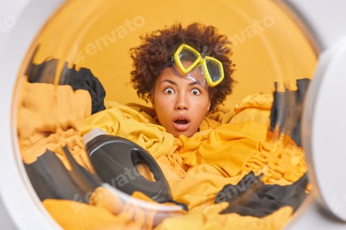 Vista previa: Scared Frightened Curly Haired Woman Wears Snorkeling Mask On Forehead Drowned In Laundry With