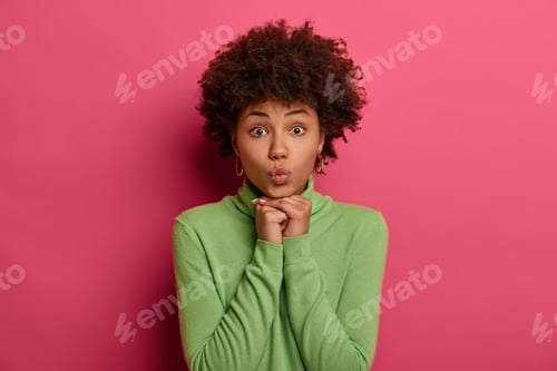 Preview: Good Looking Young Ethnic Woman Keeps Lips Rounded, Keeps Hands Under Chin, Looks Directly At