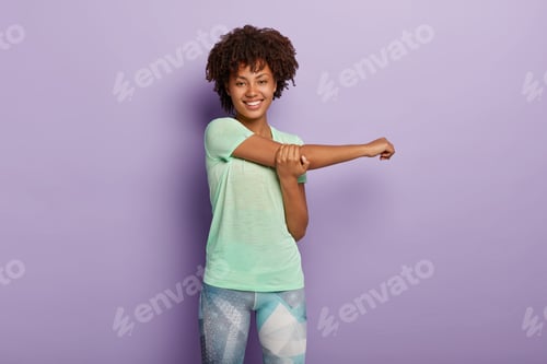 Preview: Horizontal Shot Of Happy Afro American Sporty Woman Stretches Hands Before Workout, Smiles Happily