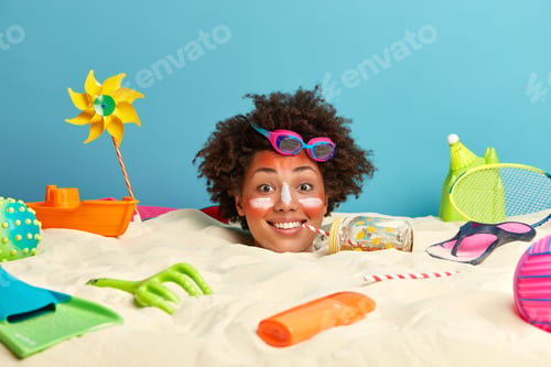 Preview: Photo Of Happy African American Woman With Curly Hair, Wears Goggles On Head, Buried In Sand