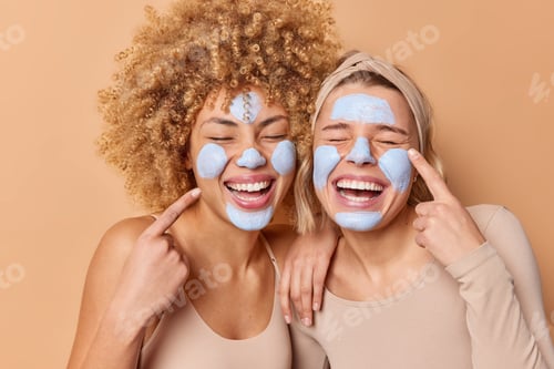 Preview: Overjoyed Women Apply Beauty Clay Mask Point Fingers At Face Stand Closely To Each Other Keep Eyes