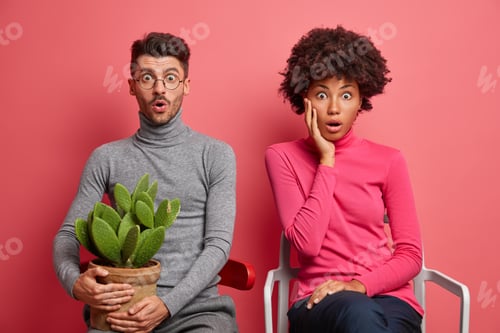 Preview: Shocked Mixed Race Young Woman And Man Sit Next To Each Other Impressed By Shocking News Pose On