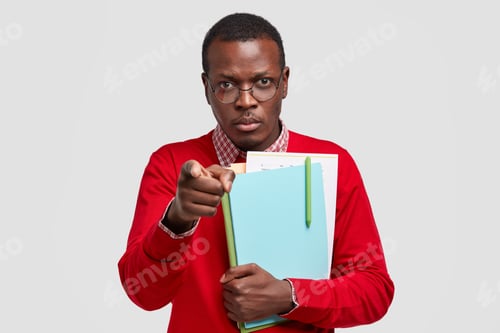 Preview: Indoor Shot Of Attractive Black Man With Serious Facial Expression, Points With Index Finger At