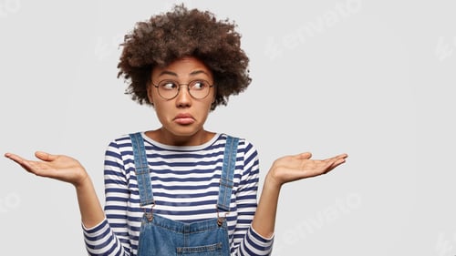 Preview: Hesitant Puzzled Young Female With Afro Haircut, Shruggs Shoulders And Faces Dilemma, Looks