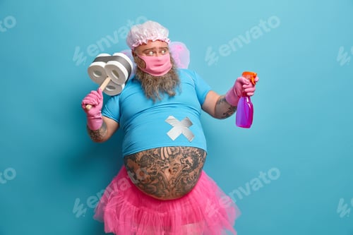 Preview: Household Concept. Bearded Overweight Adult Man Wears Protective Mask, Uses Detergent To Clean
