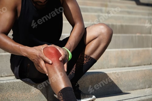 Preview: Close Up Shot Of African Athlete In Black Training Socks And Shoes Clutching His Injured Knee