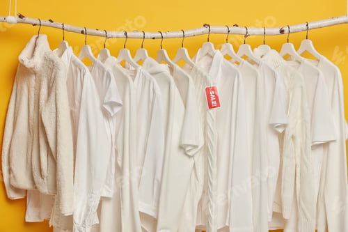 Preview: Clearance Sale Of White Clothes On Hangers Isolated Over Yellow Background. Selection Of Fashion