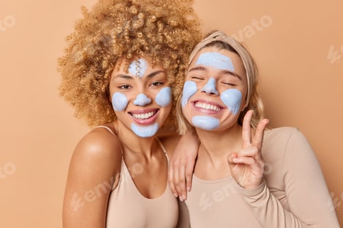 Preview: Positive Carefree Young Women With Beauty Nourishing Mask On Face Stand Closely To Each Other Smile
