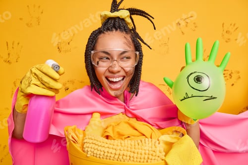 Preview: Positive Dark Skinned Female Superhero Wears Transparent Glasses And Cape Smiles Broadly Holds