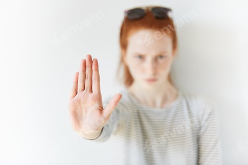 Preview: Isolated Headshot Of Serious Young Redhead Woman Showing Stop Sign. Female Wearing Striped Top