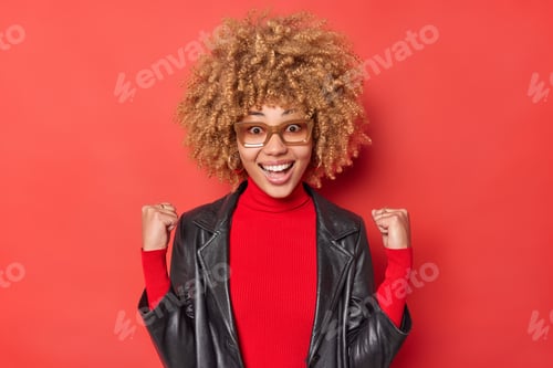 Preview: Positive Curly Haired Woman Exlclaims From Joy Clenches Fists With Triumph Wears Turtleneck And