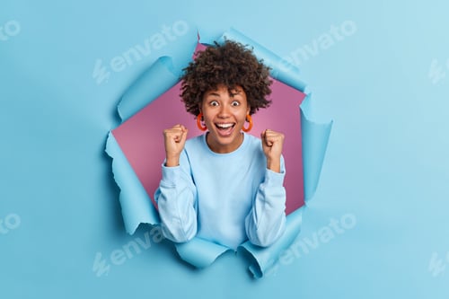 Preview: Yes Finally I Did It. Excited Dark Skinned Young Woman With Curly Hair Clenches Fists Celebrates