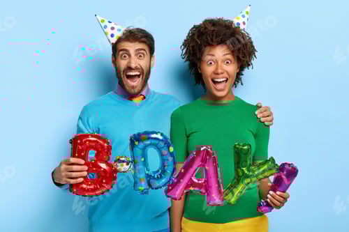 Preview: Portrait Of Overjoyed Multiethic Couple Embrace And Hold Letter Shaped Balloons, Wears Party Hats