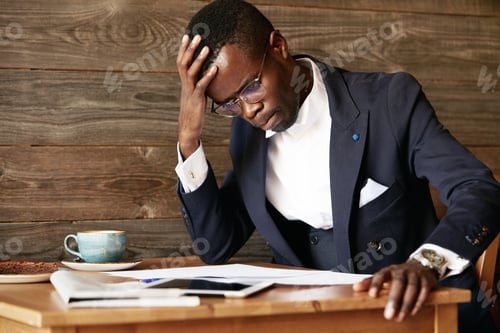 Preview: Young African Businessman Looking Puzzled, Having A Computer Problem, Sitting In Deep Thinking