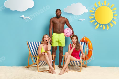 Preview: Surprised Two Women In Bathingsuit, Sit On Deckchairs, Dark Skinned Man Stands Near, Wears Green