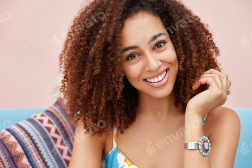 Preview: Portrait Of Glad Dark Skinned Female With Broad Pleasant Smile, Has Curly Hair And Good Rest At