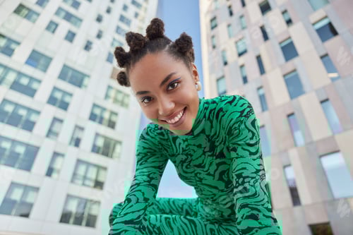 Preview: Positive Stylish Millennial Girl With Bun Hairstyle Dressed In Green Bodysuit Smiles Gladfully