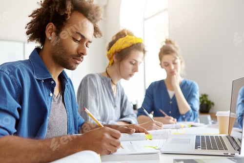 Preview: Three Multiethnic People Sitting In Light Room At Desk Working With Papers Having Takeaway Coffee