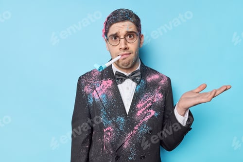 Preview: Hesitant Confused Man Shrugs Shoulders Raises Palm Whistles Party Horn Dressed In Festive Clothes