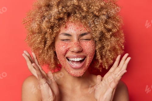 Preview: Close Up Shot Of Overjoyed Cheerful Curly Haired Young Woman Applies Natural Salt Scrub On Face To