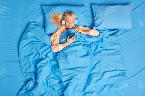 Preview: Relaxed Middle Aged Woman Stays In Bed Has Lazy Day Watches Film On Smartphone Wears Stereo