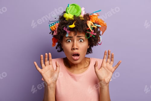 Preview: Image Of Astonished Curly Woman Collects Plastic Garbage, Raises Hands And Shows Palms, Afraid Of