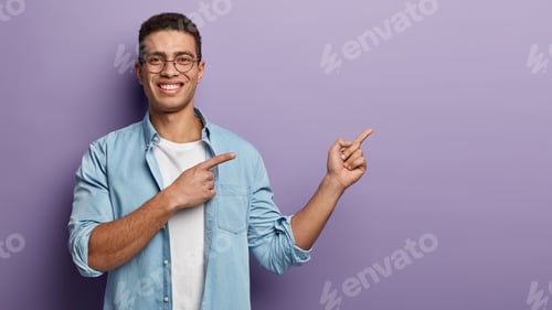 Preview: Positive Glad Handsome Guy Points Rightside On Blank Copy Space, Smiles Happily, Dressed In Blue