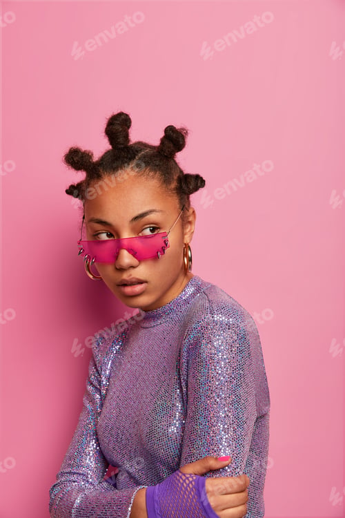 Preview: Studio Shot Of Serious Dark Skinned Teenager With Bun Hairstyle, Crosses Hands Over Body, Wears
