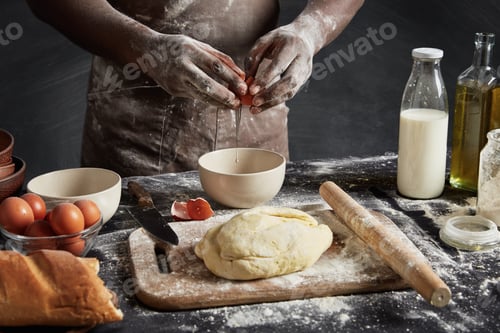 Preview: Cropped Shot Of Talented Male Cook Breaks Egg In Bowl, Has Dirty Hands And Apron After Making Dough
