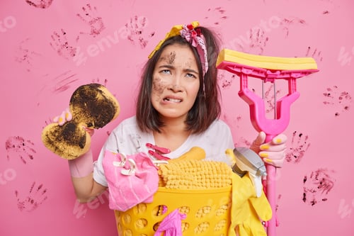 Preview: Unhappy Tired Young Asian Woman Bites Lips Looks Displeased Upwards Smeared With Dirt Holds Sponge