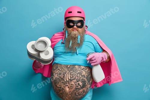 Preview: Displeased Annoyed Bearded Plump Man Dressed In Superhero Costume Holds Bottle Of Cleaning