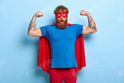 Preview: Confident Red Head Male Superhero Wears Mask And Red Cape, Raises Arms, Shows Muscles, Represents