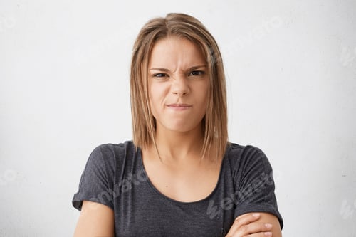 Preview: Angry Young Female With Dark Eyes Frowning Her Nose And Lips Wearing Casual T-Shirt Standing