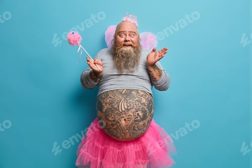 Preview: Funny Happy Bearded Man Has Image Of Fairy Holds Magic Wand Poses With Big Tattooed Belly Over Blue