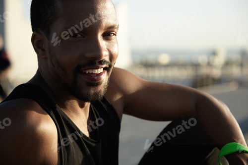 Preview: Handsome Dark-Skinned Runner Resting At Seaside After Activity In Open Air Sitting On Embankment
