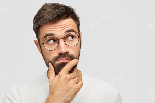 Preview: Headshot Of Serious Pensive Bearded Male With Thick Stubble, Holds Chin And Looks Pensively Aside