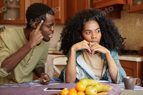Preview: Couple Having Dispute. Annoyed Beautiful Dark-Skinned Female Sitting At Kitchen Table, Ignoring